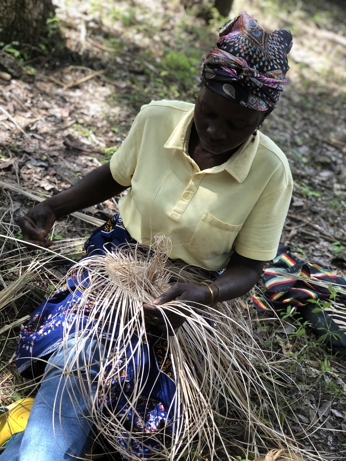 A woman weaves palm-leaf baskets in the shade of the Miombo forest